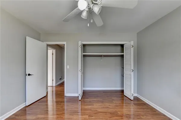 a view of an empty room with wooden floor and a ceiling fan