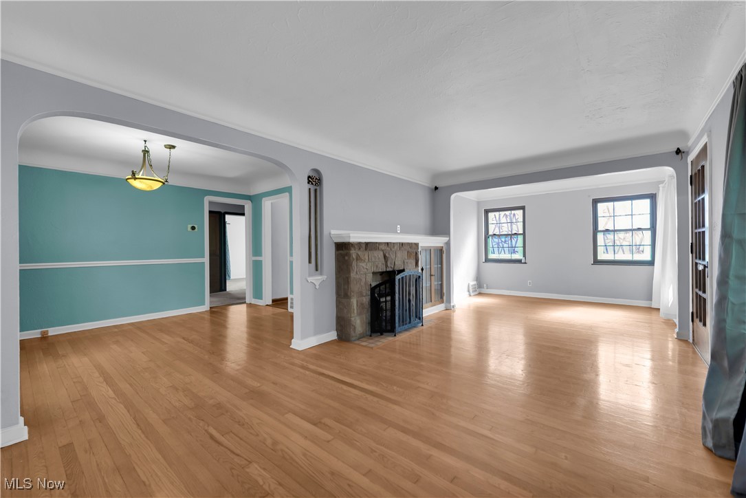 3739 Warren Road Cleveland, OH 44111 - Photo 34 of 40 Unfurnished living room with light wood-style flooring, a stone fireplace, arched walkways, and ornamental molding