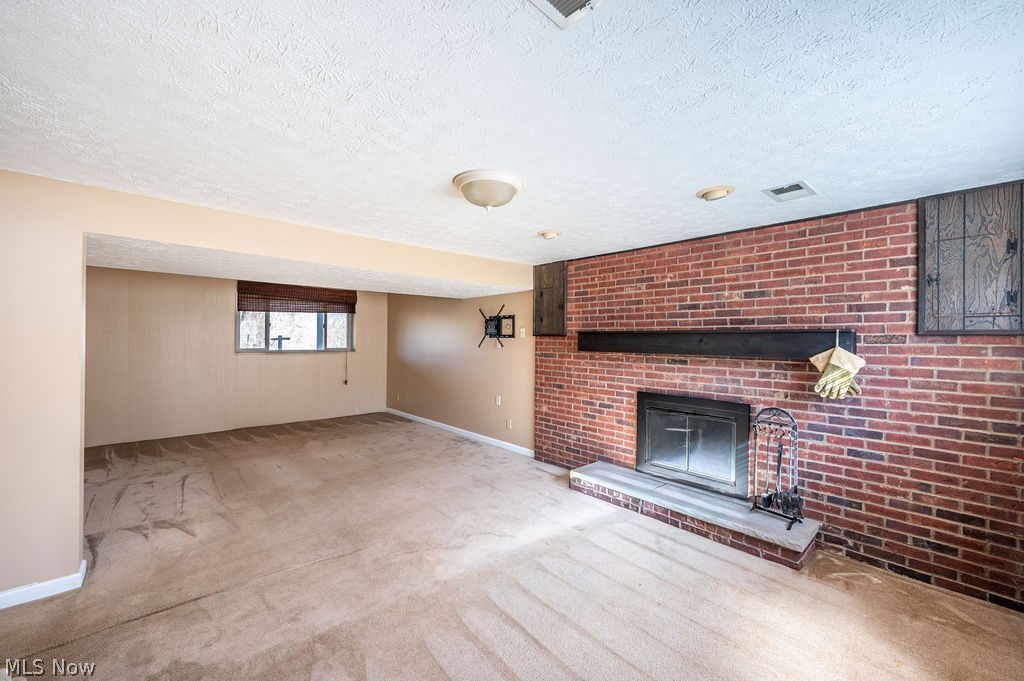 3601 River Road Vienna, WV 26105 - Photo 25 of 40 Unfurnished rec room with a textured ceiling, a brick fireplace, and light colored carpet