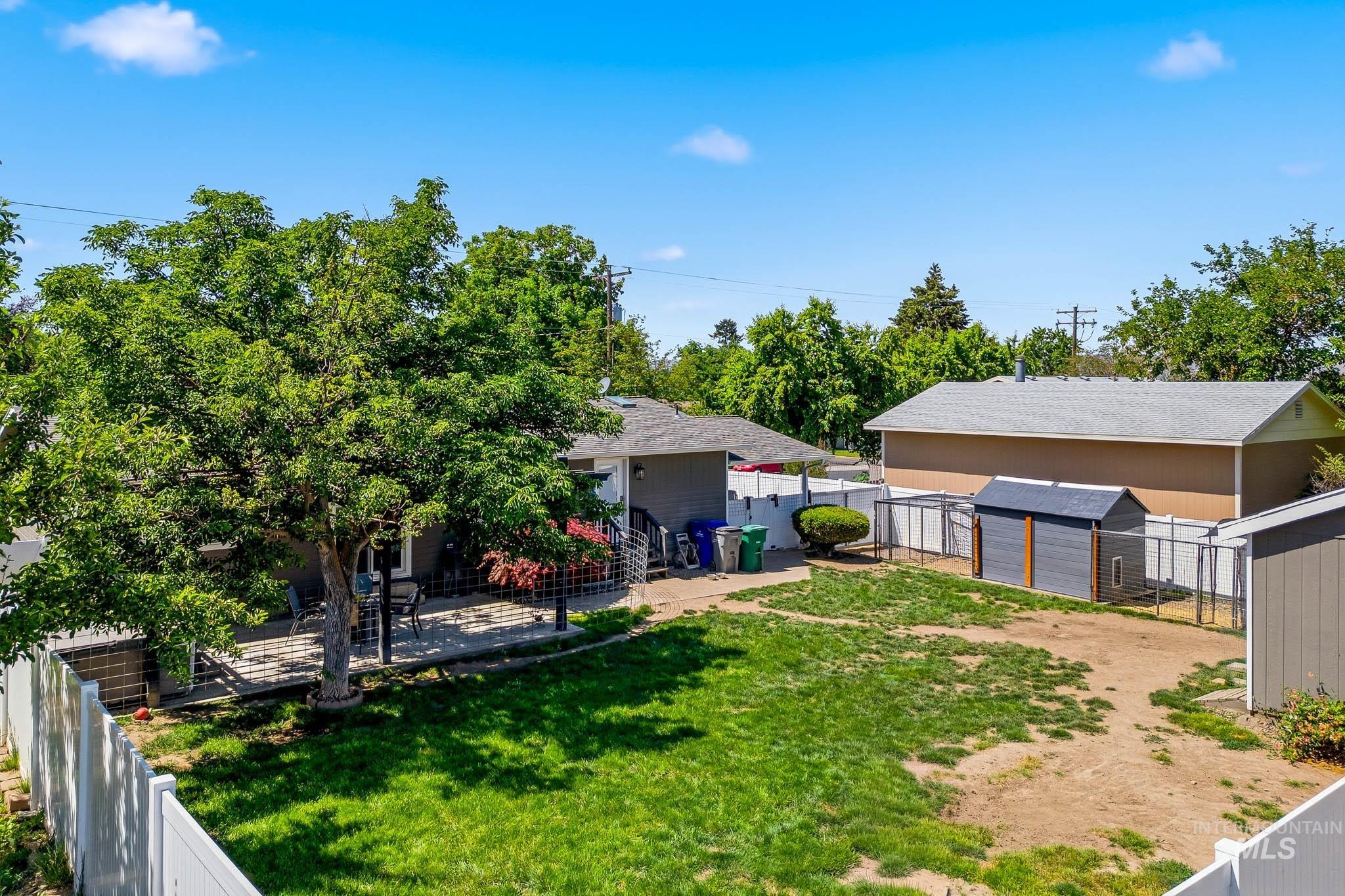 3715 18th Street Lewiston, ID 83501 - Photo 22 of 30 Expansive backyard featuring a large tree, a paved patio area, a white vinyl fence, and two storage sheds