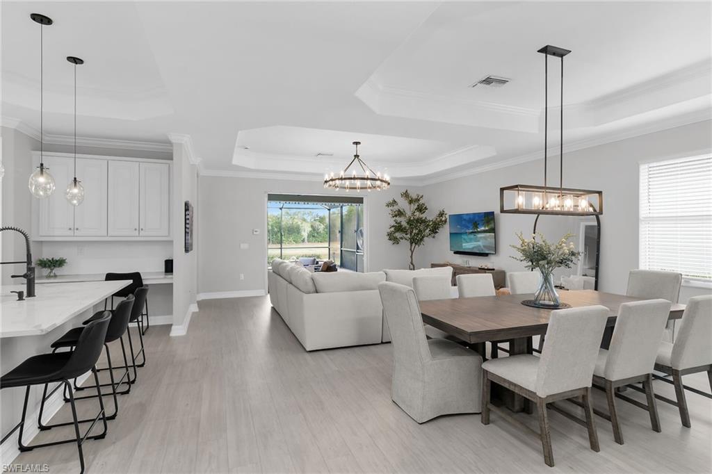 Dining room with a tray ceiling, hanging lights, light wood finished floors, and crown molding