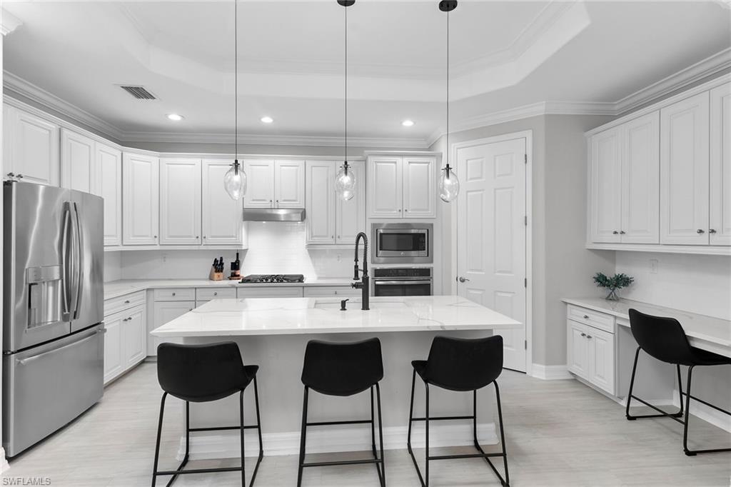 2926 Aviamar Circle Naples, FL 34114 - Photo 12 of 44 Kitchen featuring stainless steel appliances, white cabinetry, a breakfast bar area, crown molding, and a tray ceiling