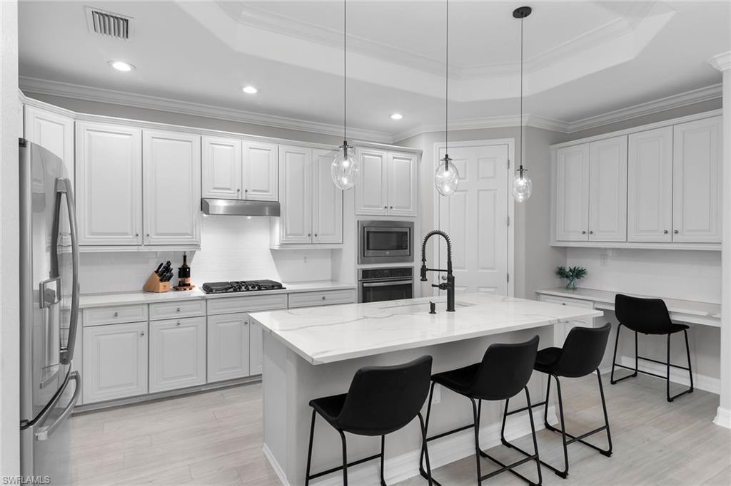 2926 Aviamar Circle Naples, FL 34114 - Photo 4 of 44 Kitchen featuring a kitchen bar, white cabinetry, stainless steel appliances, crown molding, and light wood-type flooring