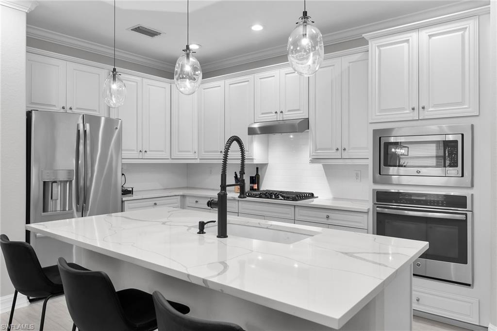 2926 Aviamar Circle Naples, FL 34114 - Photo 5 of 44 Kitchen featuring stainless steel appliances, an island with sink, light stone countertops, a breakfast bar area, and white cabinetry