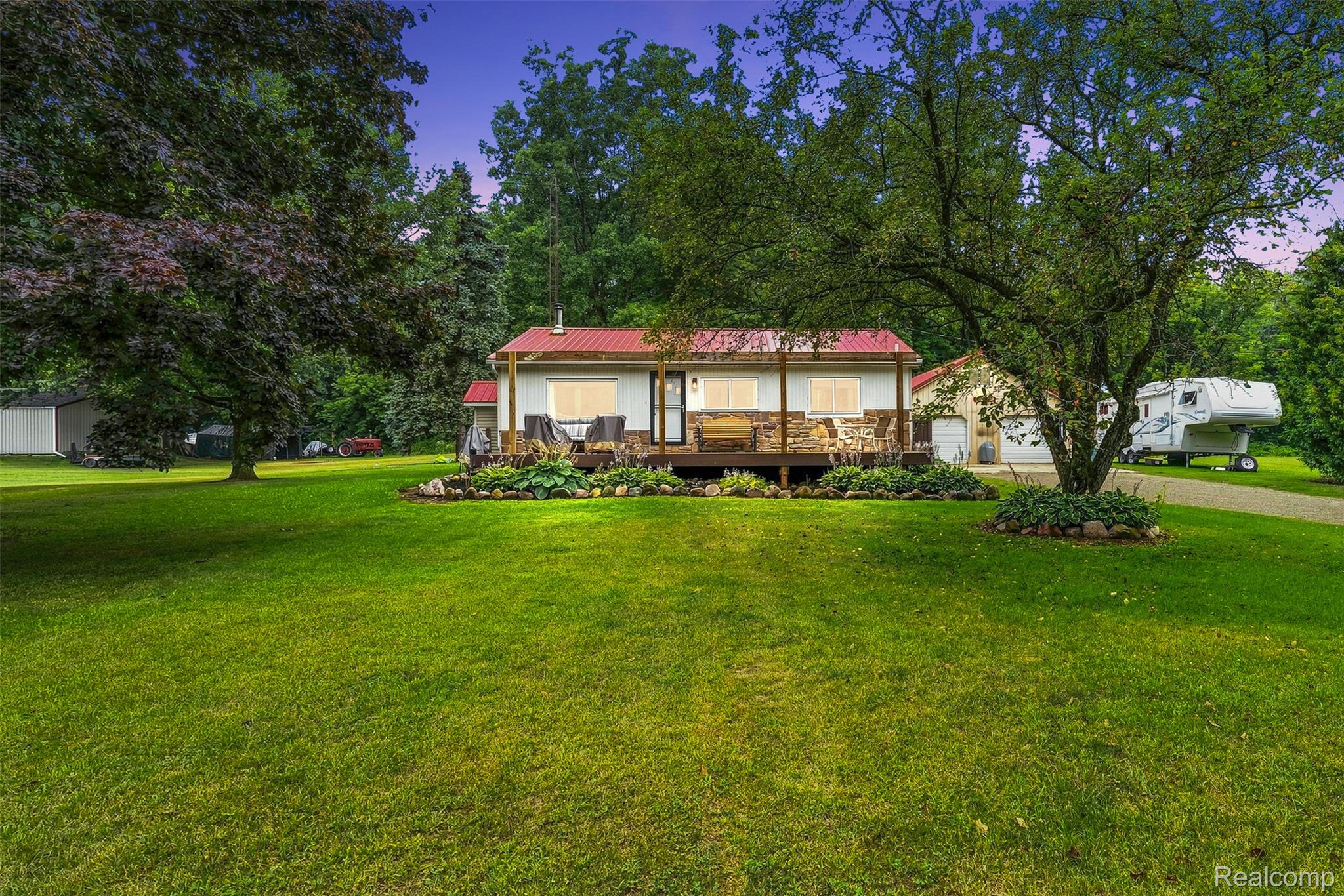 3319 Valentine Road Lapeer, MI 48446 - Photo 39 of 39 Red metal roof residence with a covered porch, stone veneer siding, and a detached two-car garage