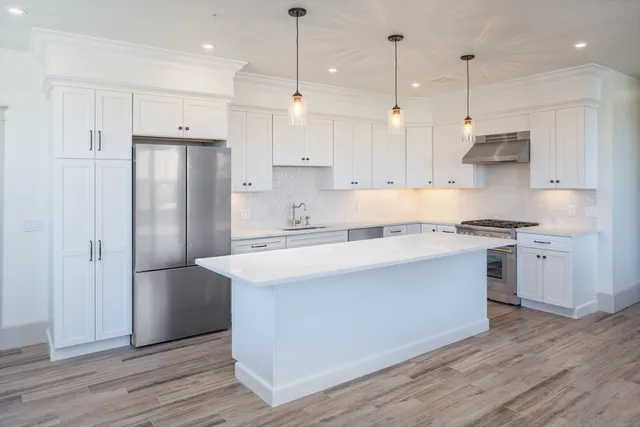 a kitchen with stainless steel appliances granite countertop a refrigerator a sink dishwasher a stove and white cabinets with wooden floor