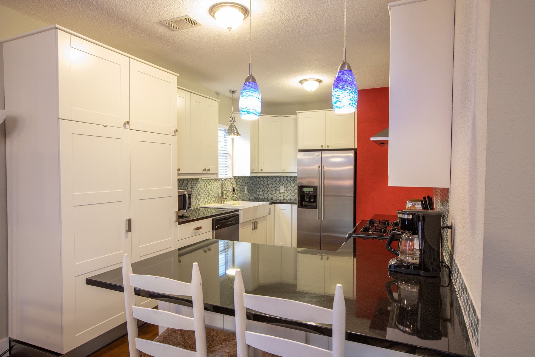 702 West N Loop Boulevard Austin, TX 78751 - Photo 10 of 23 A contemporary kitchen showcasing white cabinetry, dark granite counters, and pendant lighting over a breakfast bar.