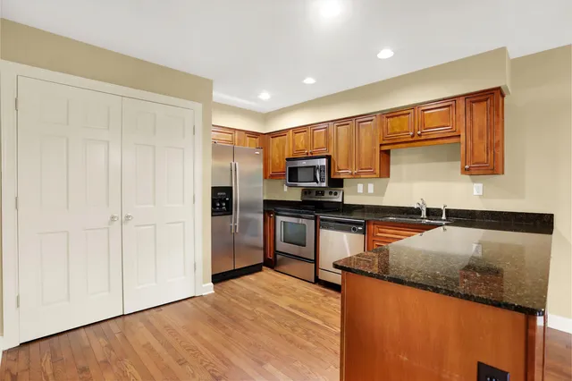 a kitchen with stainless steel appliances granite countertop a refrigerator a stove and a sink with wooden floor