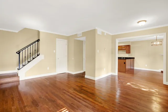 a view of an empty room with wooden floor and a kitchen