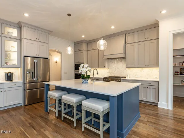 a large kitchen with stainless steel appliances a stove a sink a refrigerator and a dining table with wooden floor