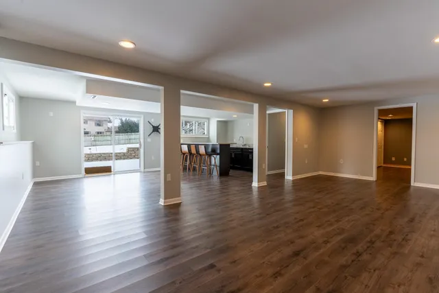 a view of an empty room with wooden floor and a kitchen