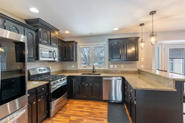 a kitchen with stainless steel appliances granite countertop wooden cabinets a sink dishwasher a stove and a refrigerator