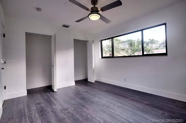 an empty room with wooden floor a ceiling fan and windows