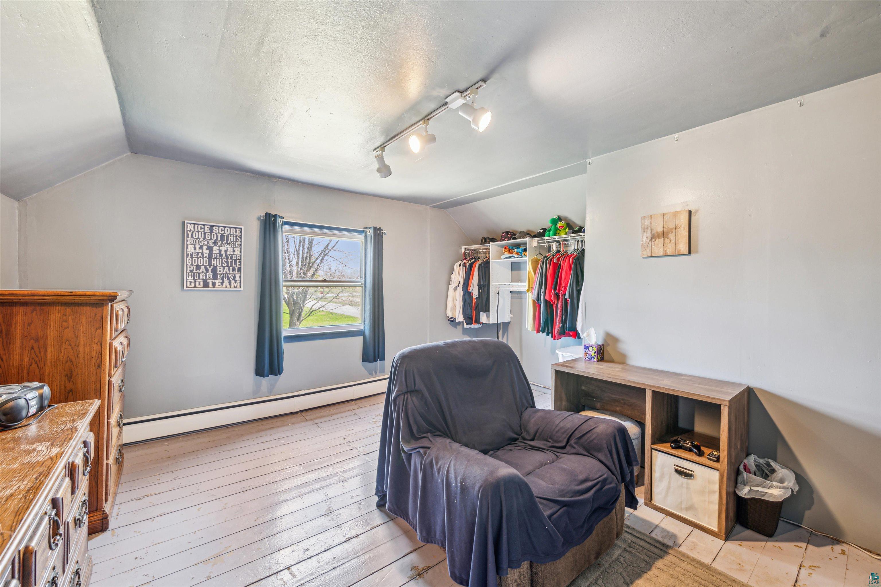 8920 School Road Port Wing, WI 54865 - Photo 19 of 27 Bedroom featuring baseboard heating, rail lighting, light wood-style flooring, vaulted ceiling, and a closet