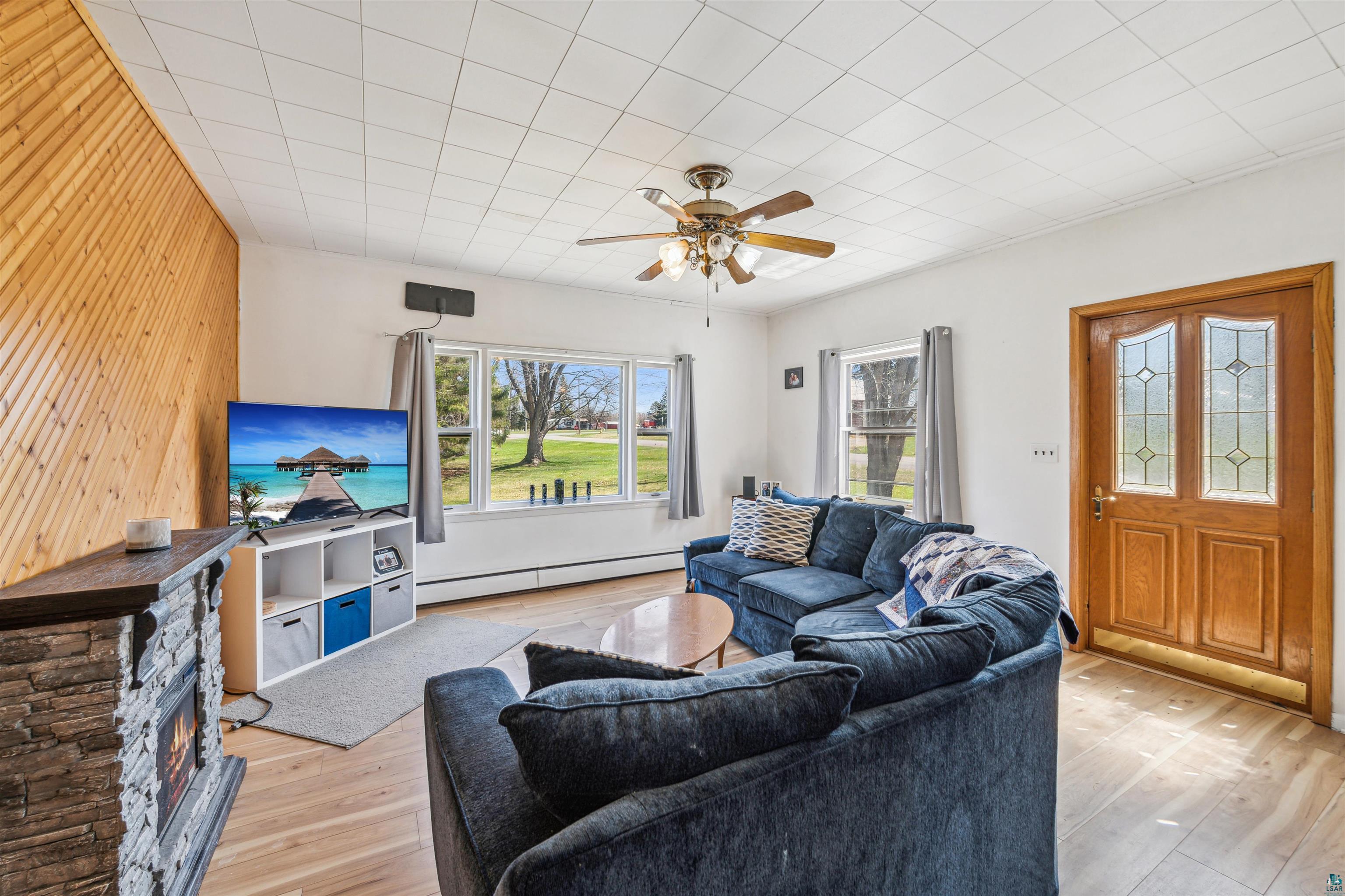 8920 School Road Port Wing, WI 54865 - Photo 9 of 27 Living room featuring ceiling fan, baseboard heating, wood walls, and light wood-style flooring