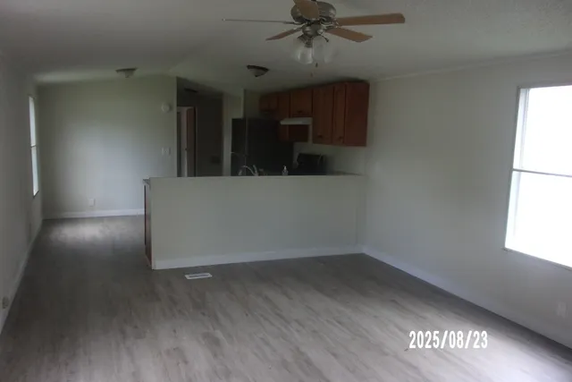 an empty room with wooden floor fan and windows