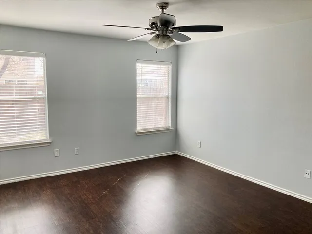 an empty room with wooden floor chandelier fan and windows