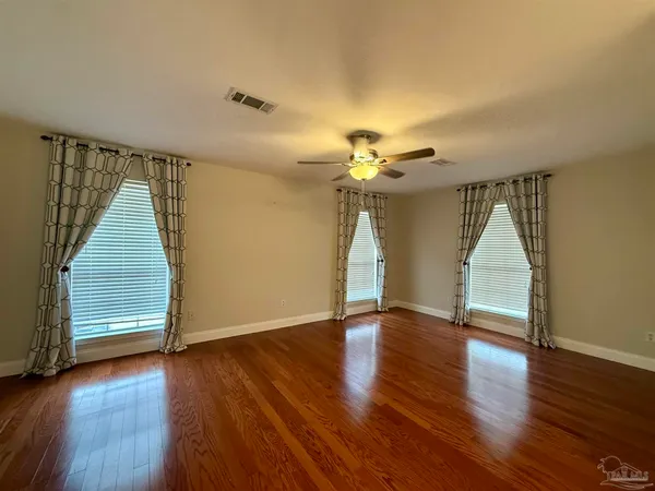 a view of an empty room with wooden floor and fan