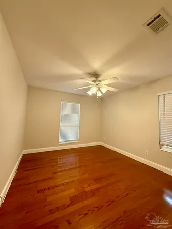 a view of an empty room with wooden floor and fan