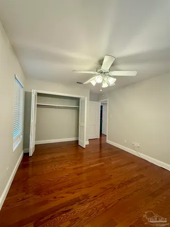 a view of an empty room with wooden floor and a ceiling fan