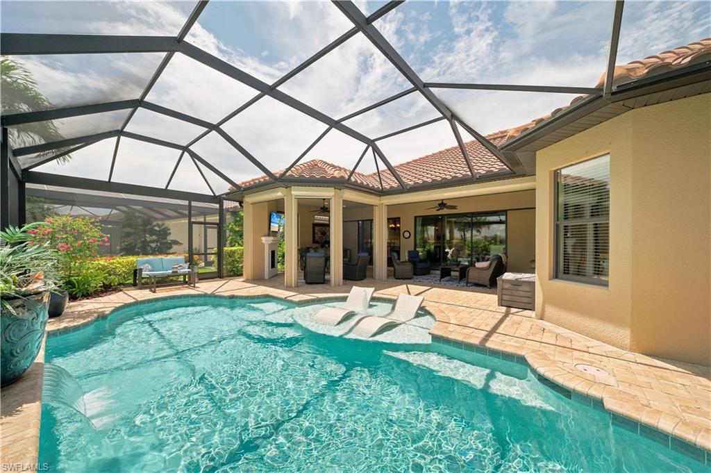 9256 Rialto Lane Naples, FL 34119 - Photo 40 of 43 Screened pool enclosure featuring a freeform pool with sun shelf and water feature, surrounded by paver decking and lush landscaping