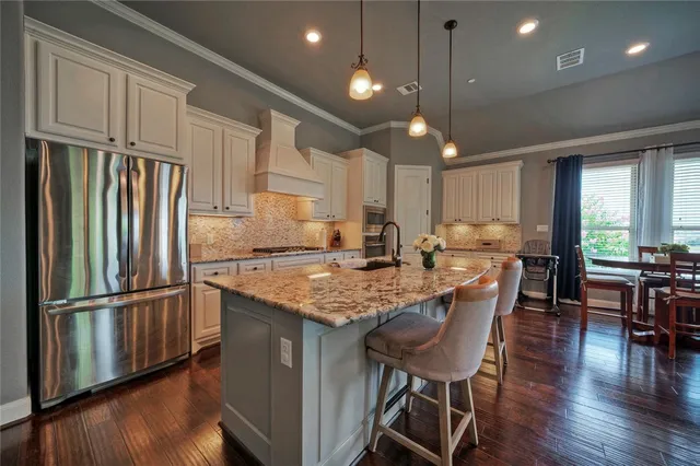 a kitchen with stainless steel appliances granite countertop a refrigerator a sink dishwasher a dining table and chairs with wooden floor