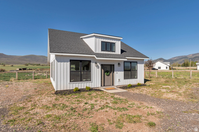 1820 West Farmhouse Flats Road Peoa, UT 84061 - Photo 59 of 79 Modern farmhouse-style exterior featuring vertical white siding, black-framed windows, a dark shingled roof, a dormer window, and a clear mountain backdrop