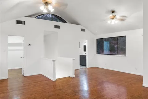 a view of an empty room with wooden floor and a ceiling fan
