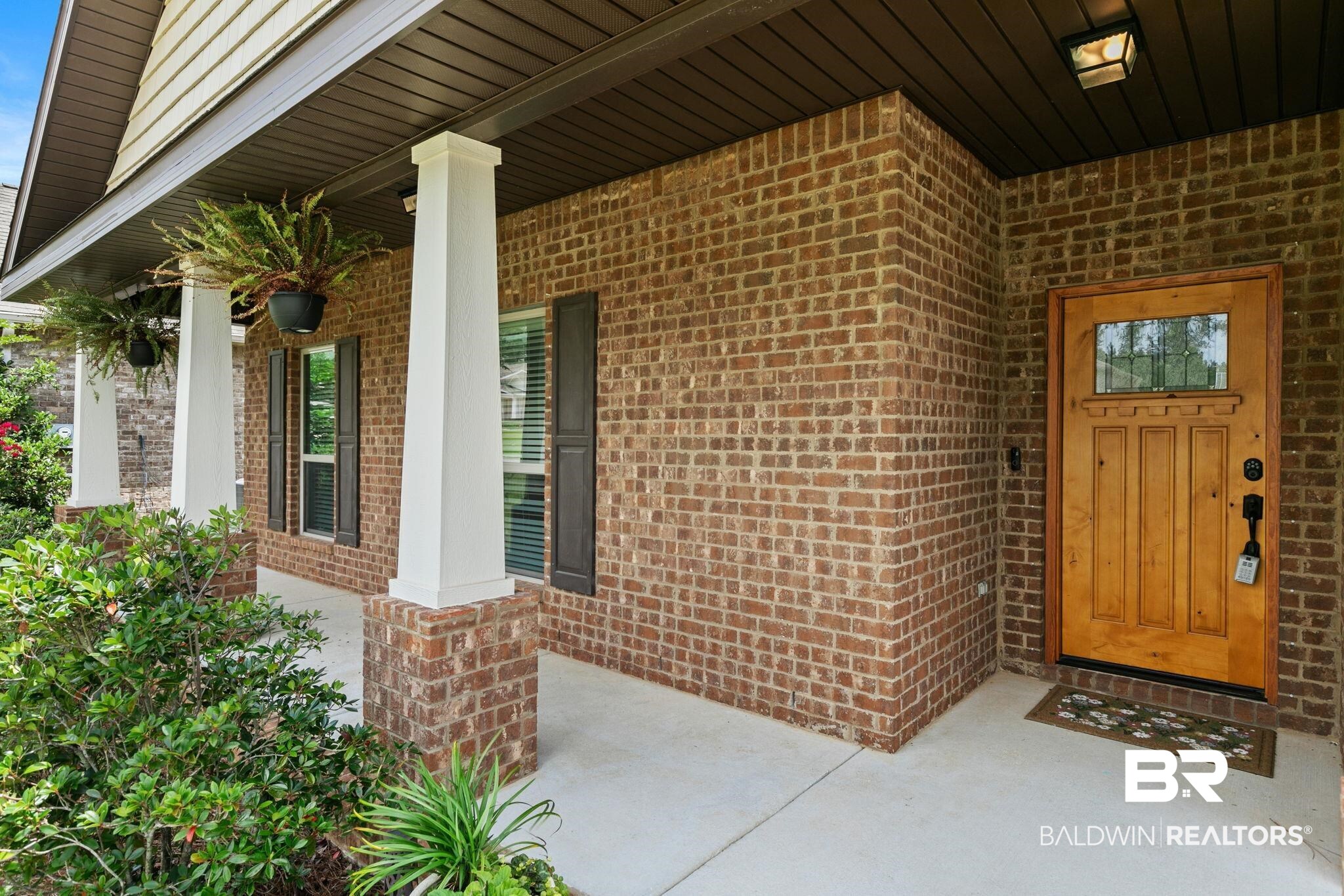 31350 Hoot Owl Road Daphne, AL 36527 - Photo 90 of 94 Brick exterior featuring a wood-panel entry door with decorative glass, a concrete porch, white support columns, and dark window shutters