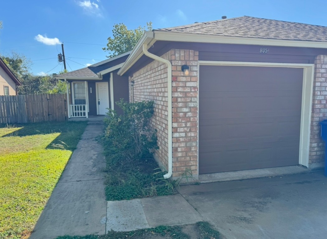 View of property exterior with brick siding, an attached garage, and a shingled roof