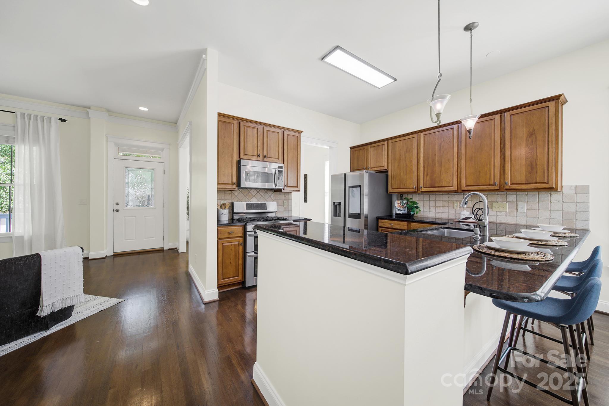 1855 2nd Baxter Crossing Fort Mill, SC 29708 - Photo 12 of 48 a kitchen with granite countertop a stove a sink a refrigerator a dining table and chairs cabinets with wooden floor