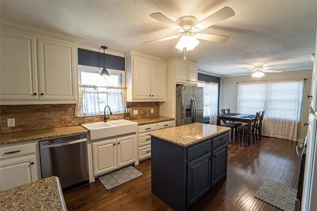 a open kitchen with stainless steel appliances granite countertop a stove top oven a sink dishwasher a dining table and chairs with wooden floor
