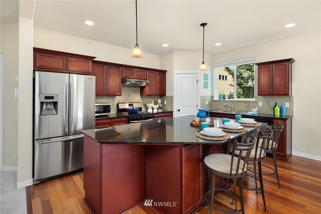 5115 Northeast 6th Place Renton, WA 98059 - Photo 11 of 26 a kitchen with stainless steel appliances granite countertop a sink a stove a refrigerator cabinets and a dining table with wooden floor