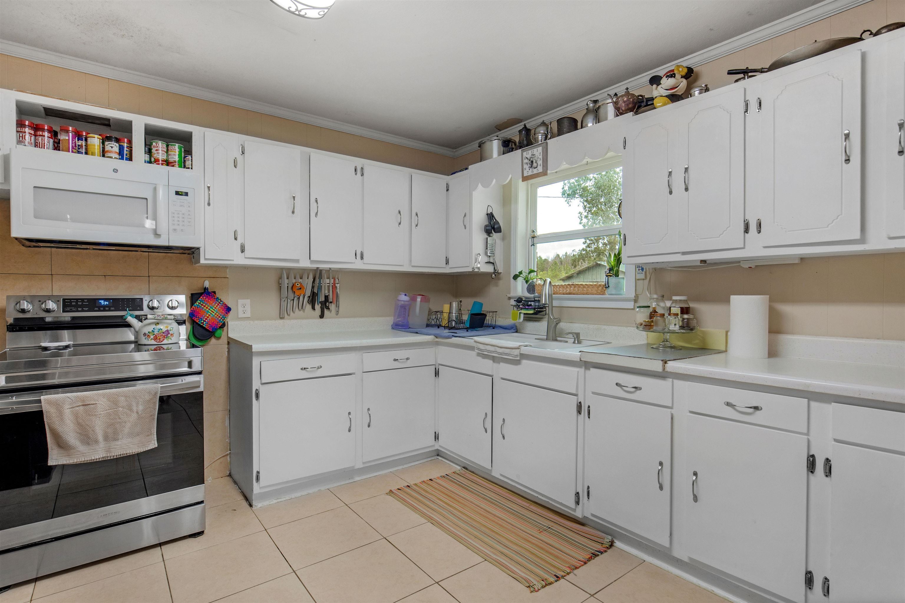1147 Mack Pond Road Atmore, AL 36502 - Photo 6 of 40 Kitchen featuring white cabinets, light tile patterned floors, electric range, sink, and ornamental molding