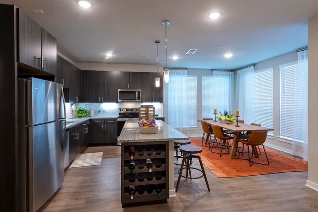 a kitchen with stainless steel appliances kitchen island granite countertop a refrigerator a stove a sink a dining table and chairs with wooden floor