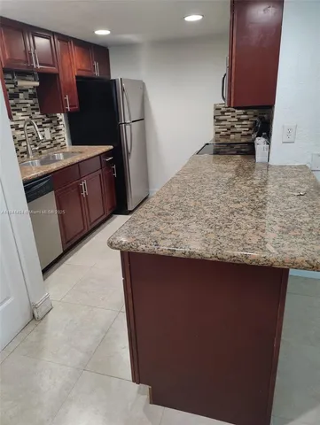 a view of kitchen island a sink a refrigerator a counter top space and cabinets