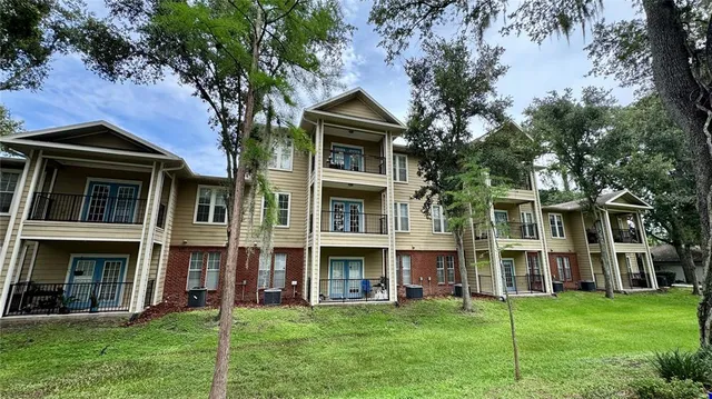 a view of an brick house with a big yard and large trees