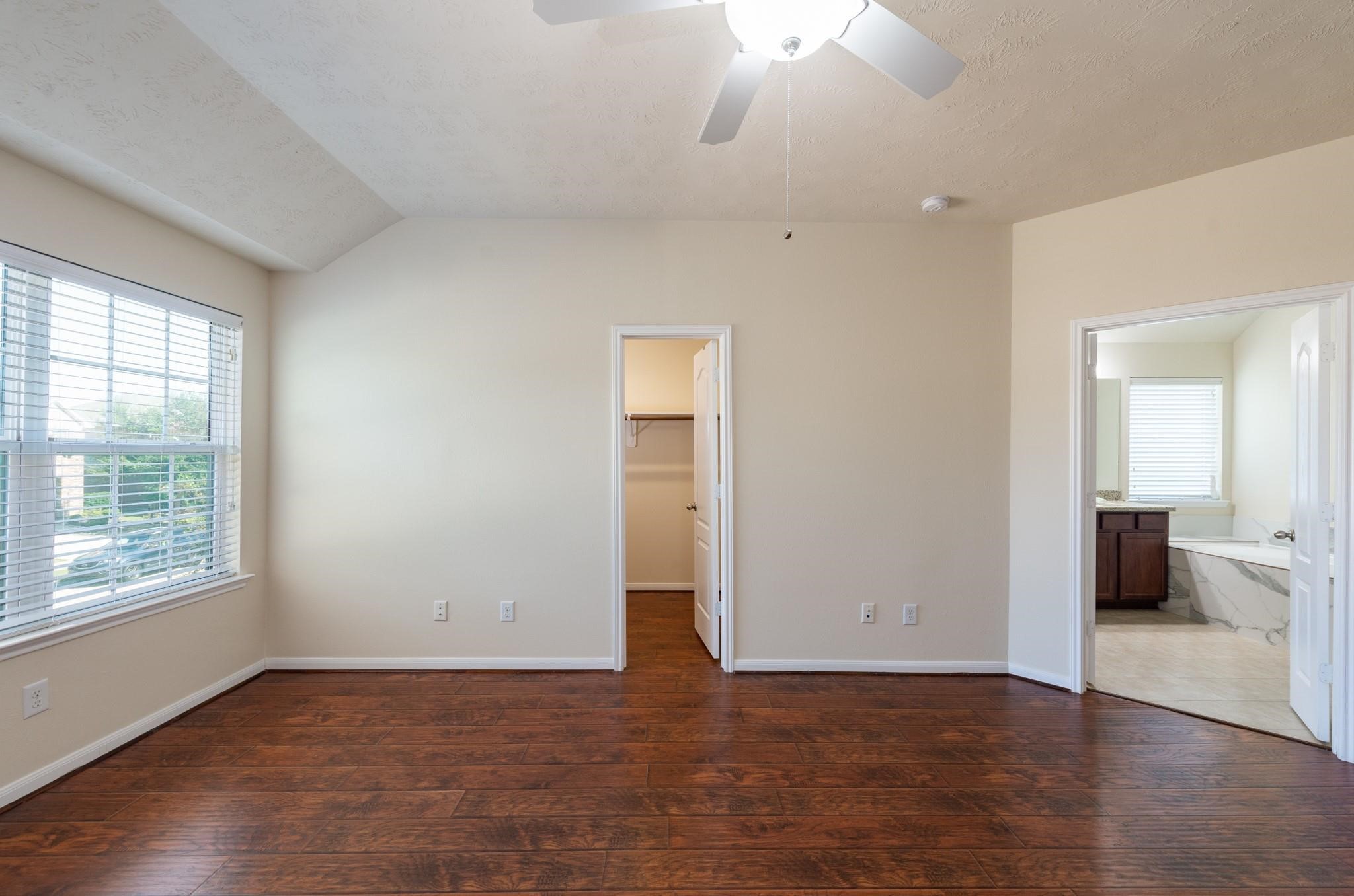 6402 Addlestone Ridge Lane Katy, TX 77494 - Photo 13 of 25 Primary suite featuring rich wood-look flooring, abundant natural light, and direct access to a private en-suite bath. The generous walk-in closet provides ample storage, creating a comfortable and functional retreat at the end of the day.