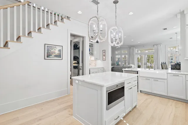a large white kitchen with a large island oven a stove and a chandelier