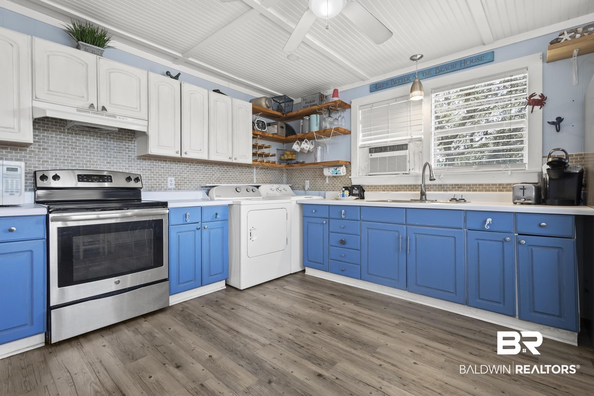 562 Veterans Road Gulf Shores, AL 36542 - Photo 5 of 32 Kitchen featuring stainless steel electric range oven, blue cabinetry, a sink, under cabinet range hood, and washer / dryer