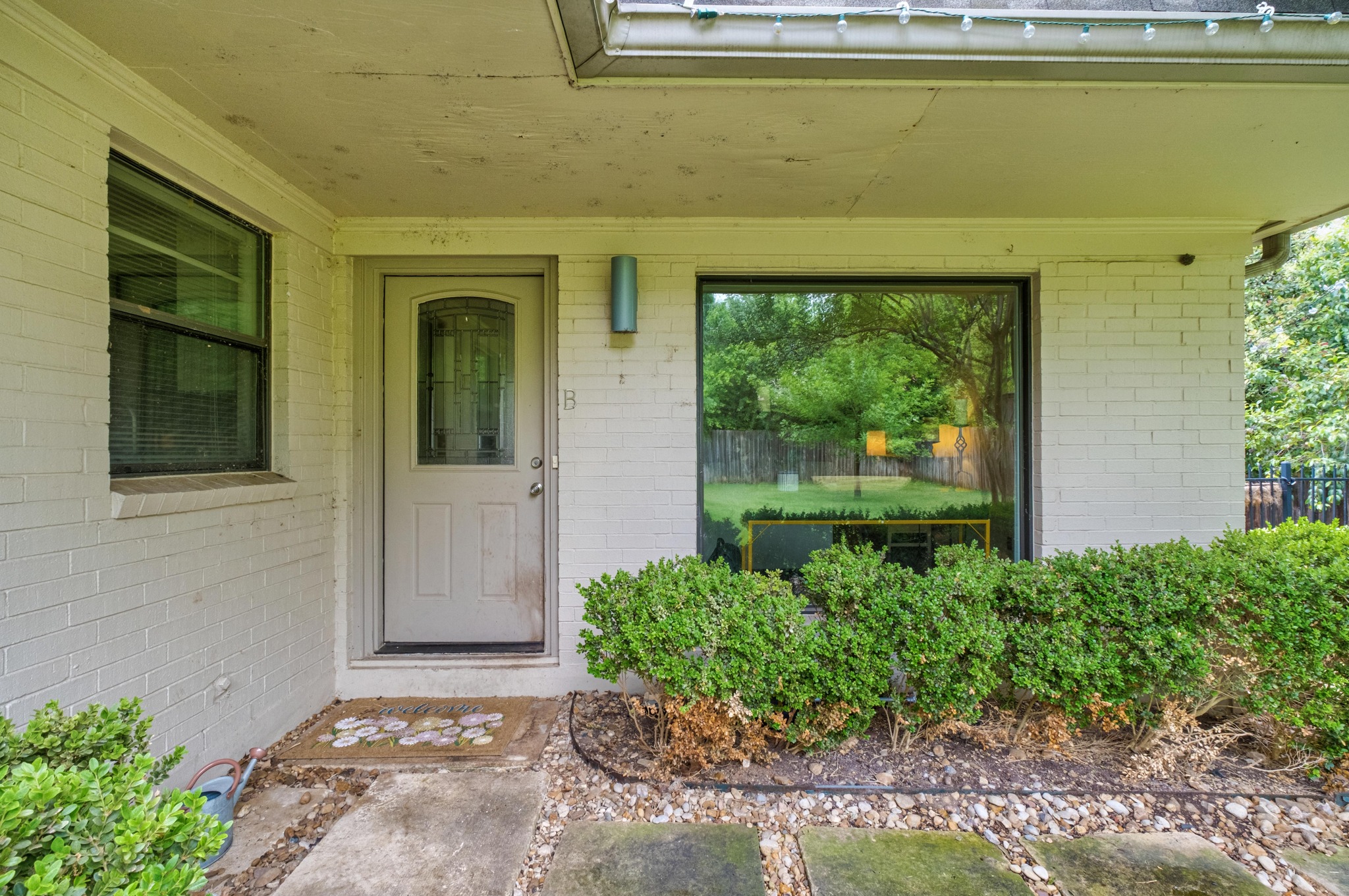 2802 Warren Street, Unit B Austin, TX 78703 - Photo 2 of 23 White brick exterior featuring an entry door with an arched glass insert, an oversized window, an exterior light fixture, and established shrubbery