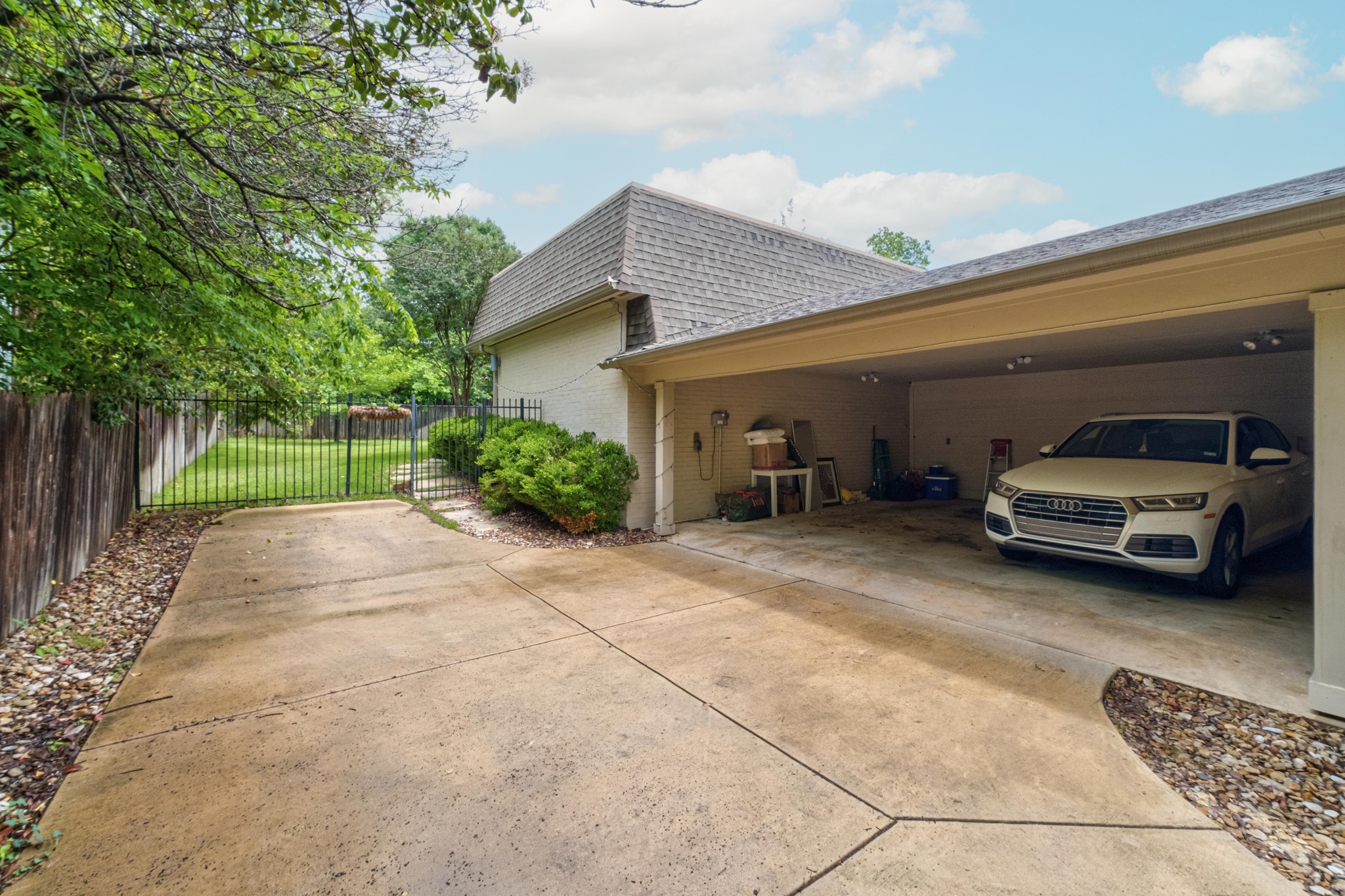 2802 Warren Street, Unit B Austin, TX 78703 - Photo 23 of 23 Covered carport parking with recessed lighting, an adjacent concrete driveway, and a gated perimeter fence leading to a grassy yard area