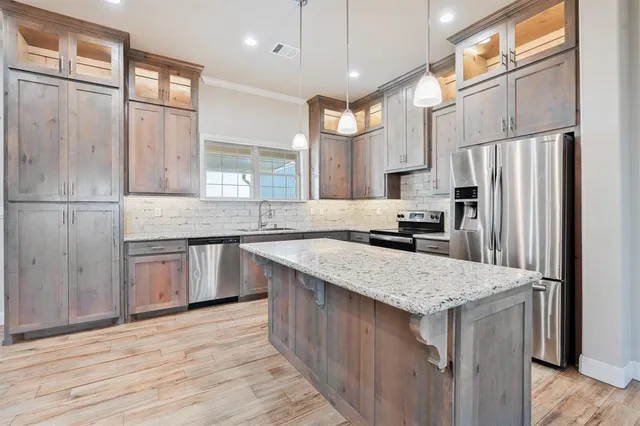 a kitchen with stainless steel appliances granite countertop a refrigerator a sink dishwasher a stove and white countertops with wooden floor