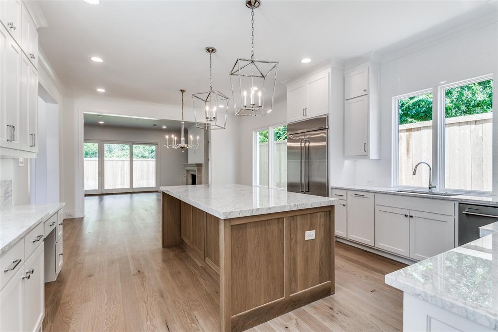 7519 Taos Road Dallas, TX 75209 - Photo 23 of 40 Kitchen with white cabinetry, light stone counters, a kitchen island, brown cabinetry, and appliances with stainless steel finishes