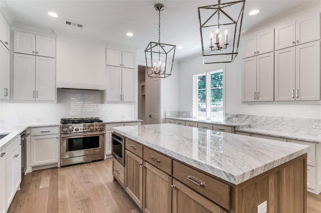 7519 Taos Road Dallas, TX 75209 - Photo 24 of 40 Kitchen featuring light wood-style floors, a center island, light stone counters, stainless steel appliances, and brown cabinets