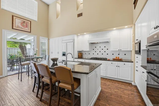 a dining hall with stainless steel appliances granite countertop a stove a sink dishwasher and a refrigerator with wooden floor