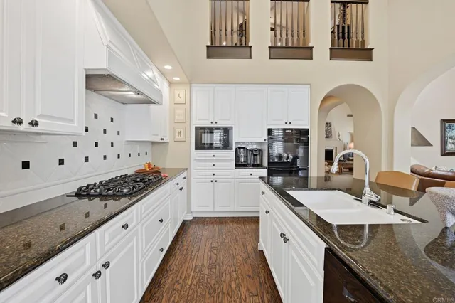 a white kitchen with stainless steel appliances granite countertop a stove and a sink