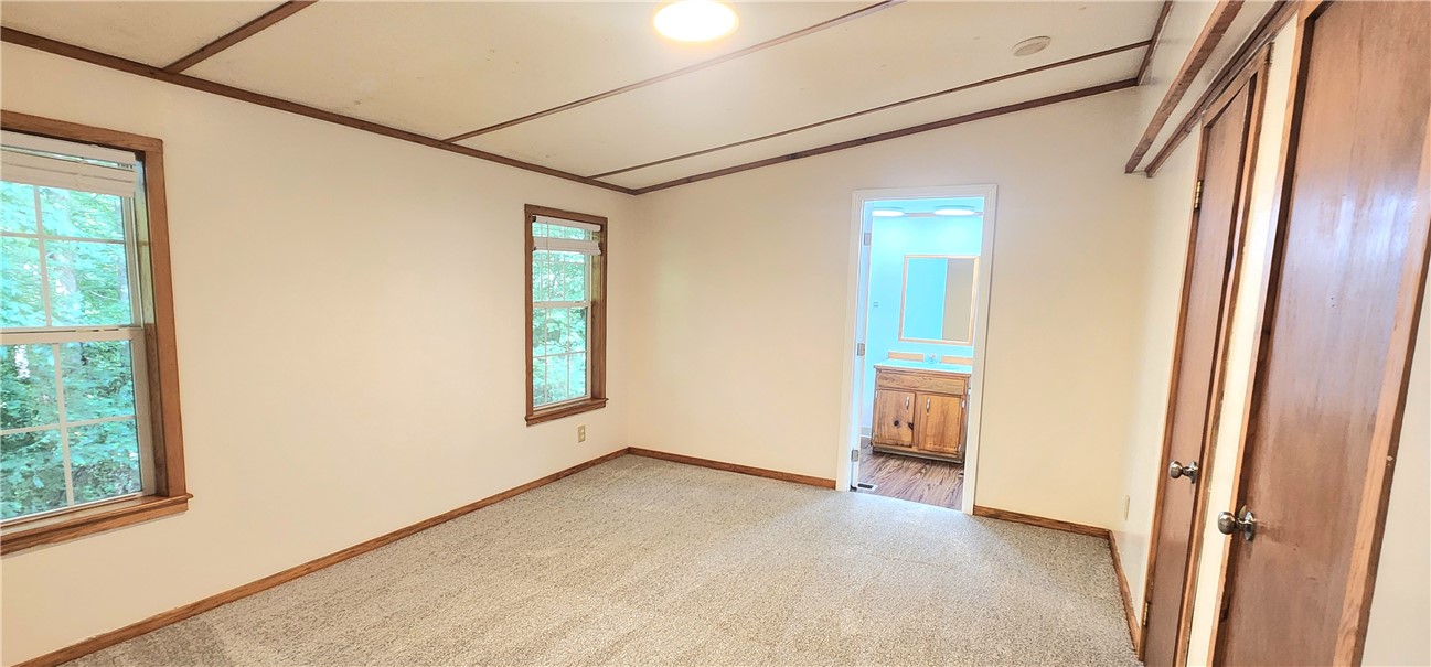 An ensuite bathroom adjoins this bedroom featuring wood-trimmed windows and new carpet