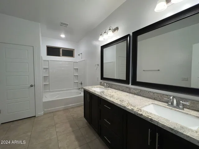 a bathroom with a granite countertop double vanity sink a mirror and a bathtub