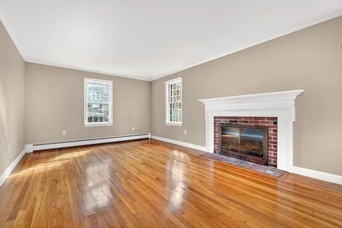 a view of an empty room with wooden floor fireplace and a window